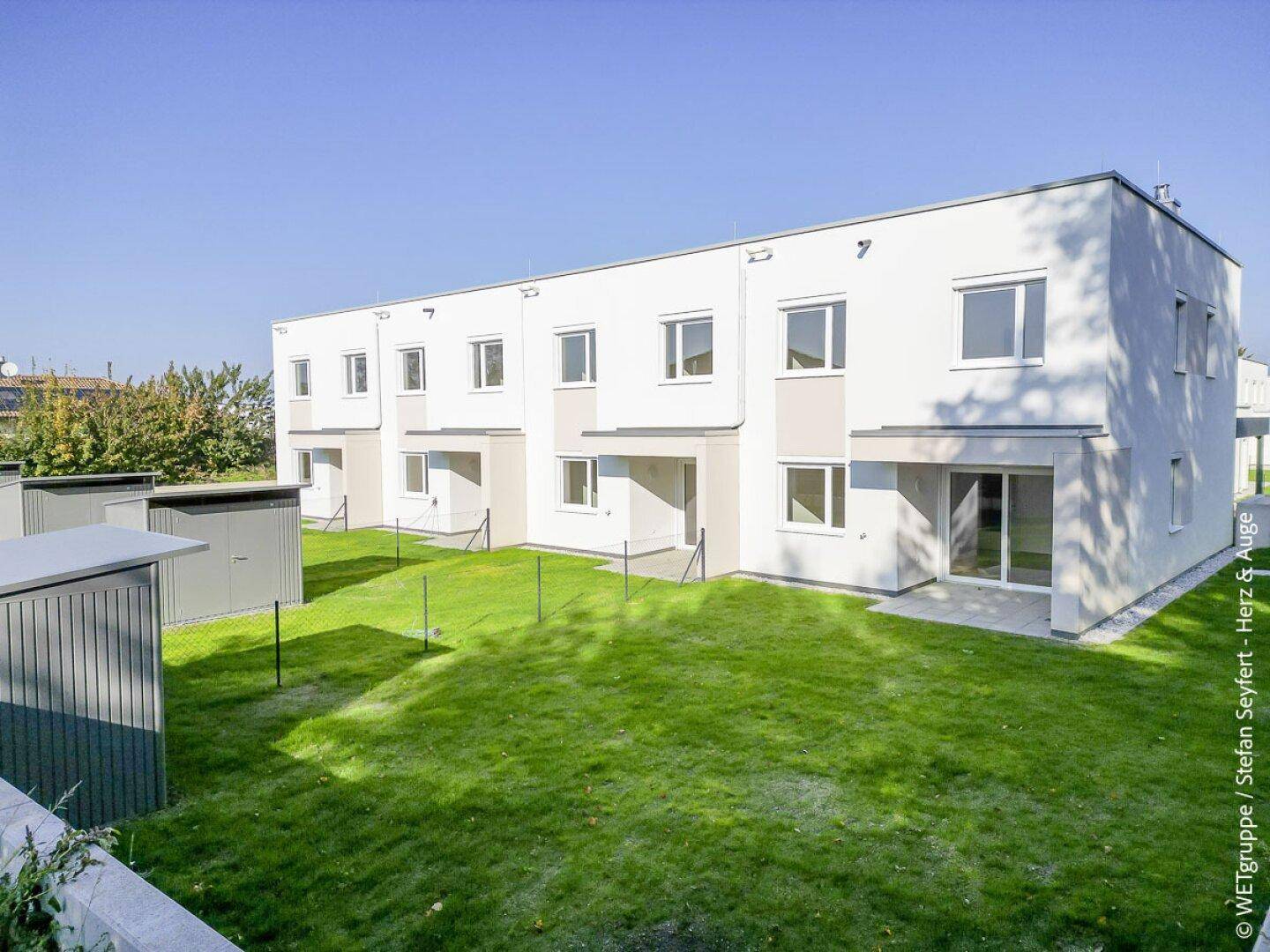 Rückseite der Reihenhäuser mit privaten Gärten, Terrassen und kleinen Gartenhäusern.