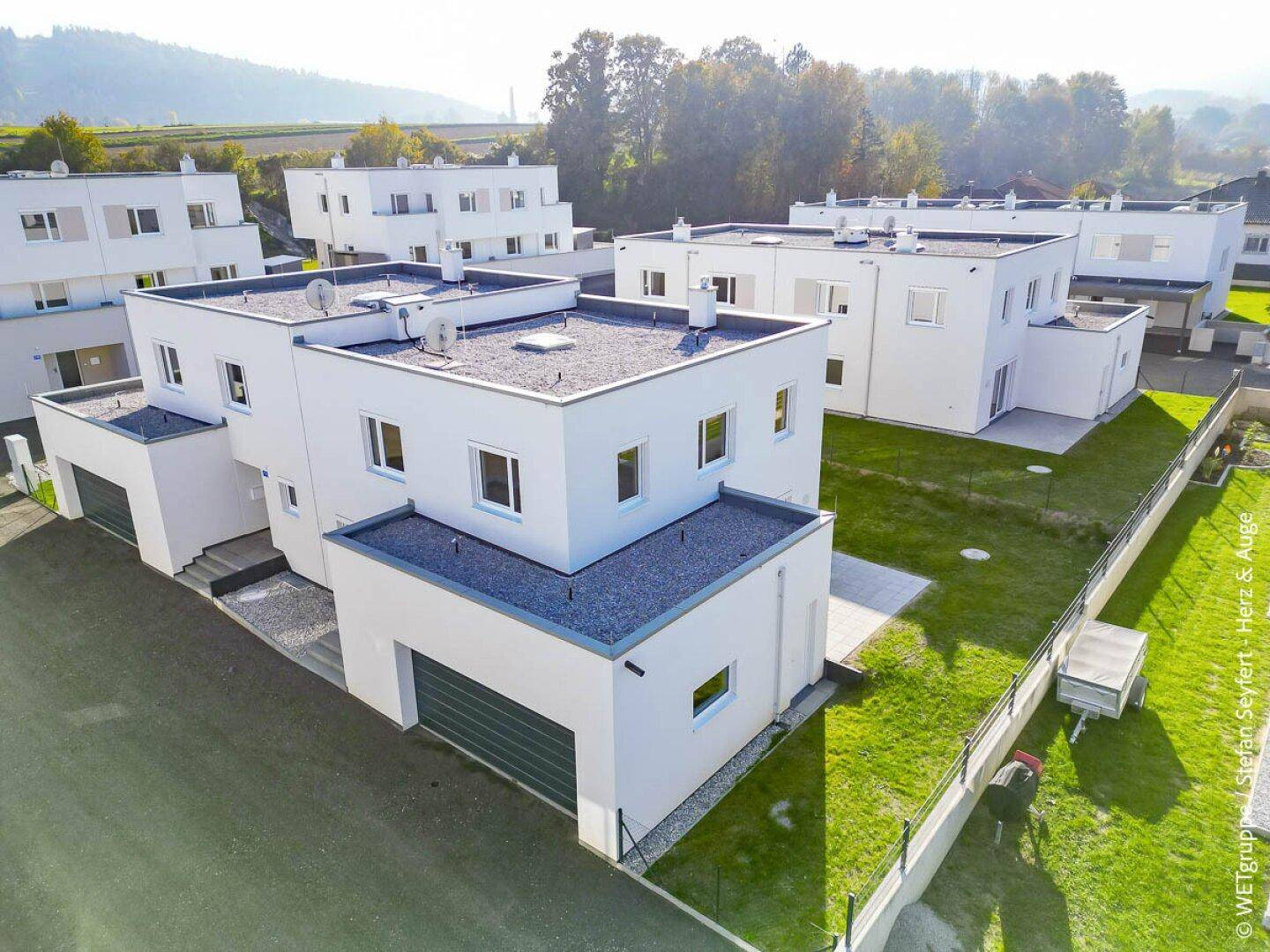 Moderne Reihenhäuser mit Flachdach, privaten Gärten und integrierten Garagen in ländlicher Umgebung.