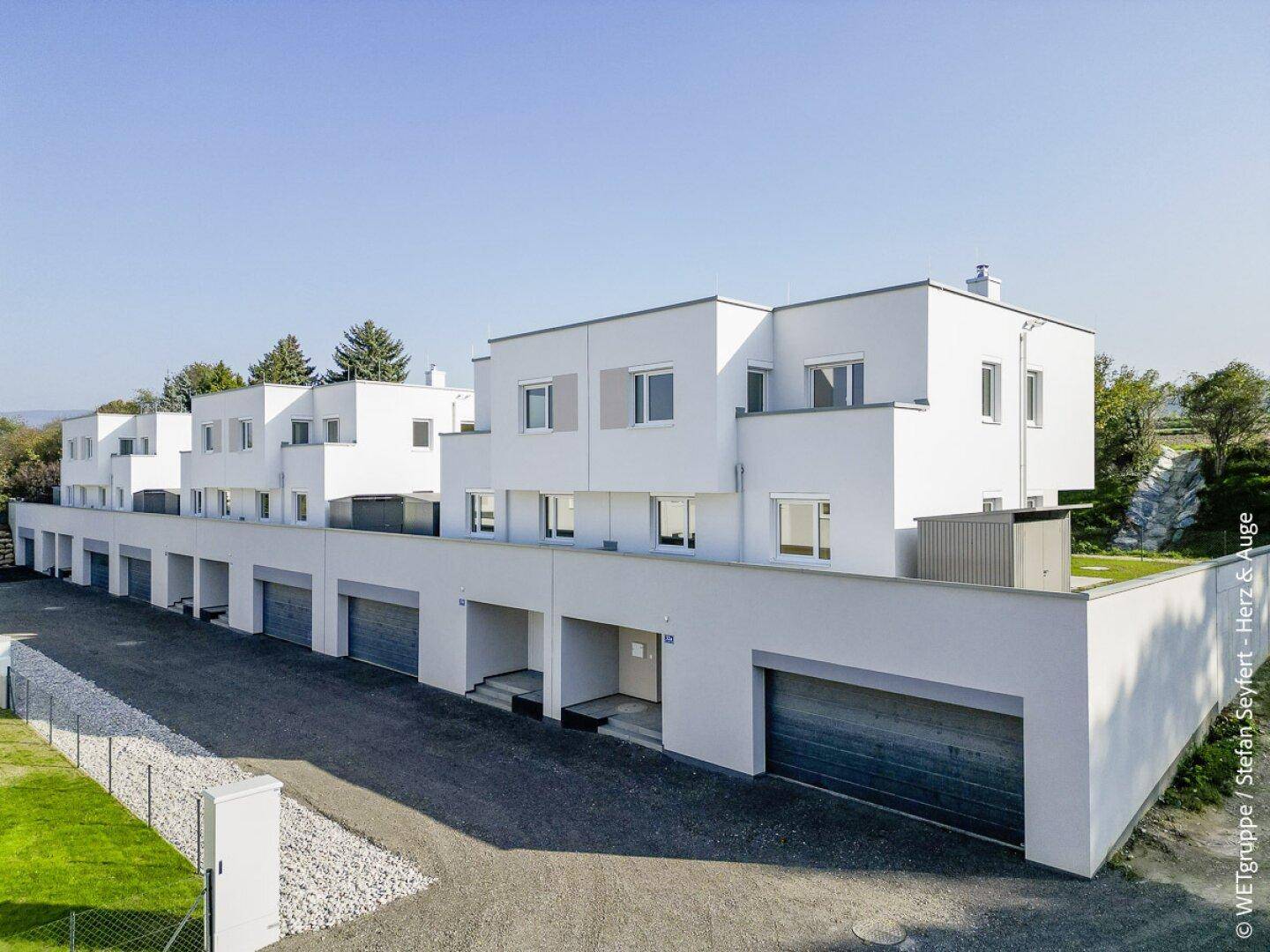 Moderne Reihenhäuser mit integrierten Garagen und Zufahrt, umgeben von Grünflächen.