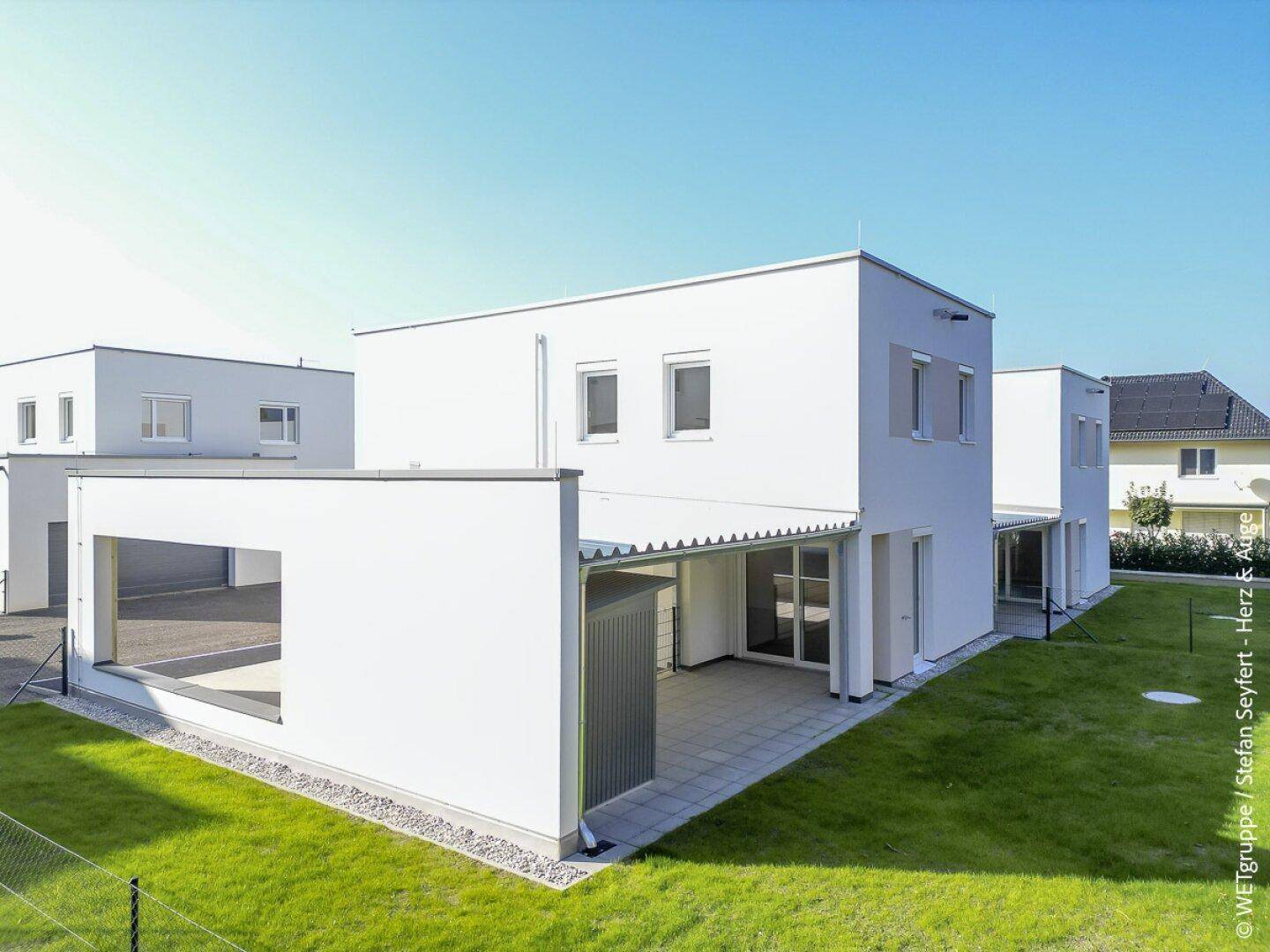 Modernes Reihenhaus mit überdachter Terrasse, angrenzendem Garten und Carport.