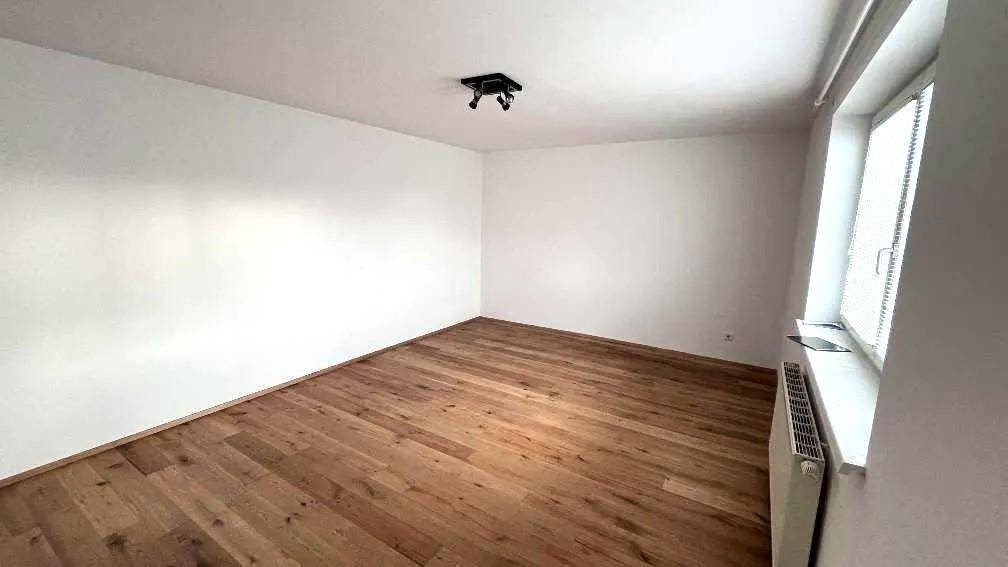 Geräumiges, leeres Schlafzimmer mit hellem Holzparkett und einem großen Fenster für natürliche Belichtung.