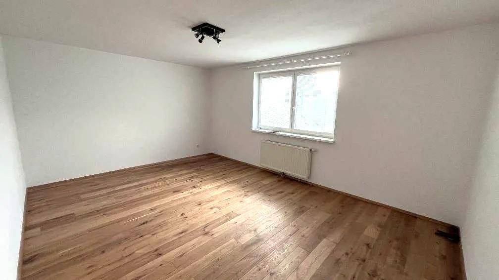 Leeres Schlafzimmer mit Holzfußboden, weißen Wänden und einem Fenster, das viel Licht hereinlässt.
