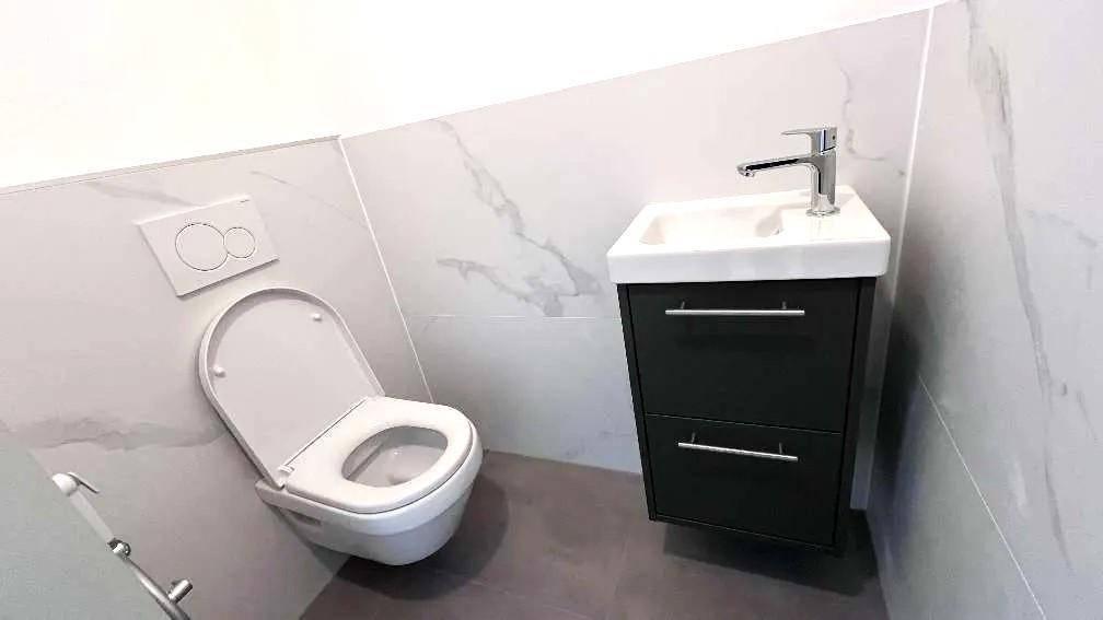 Kompaktes Gäste-WC mit wandhängender Toilette, kleinem Waschbecken und modernen Fliesen.