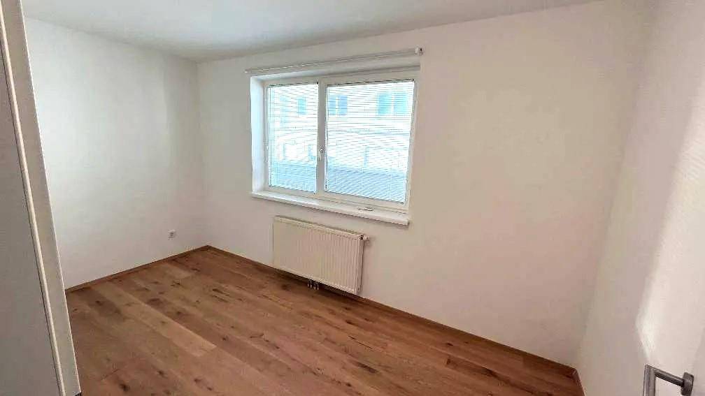 Leeres Schlafzimmer mit Holzboden und einem großen Fenster, das den Raum mit Tageslicht füllt.