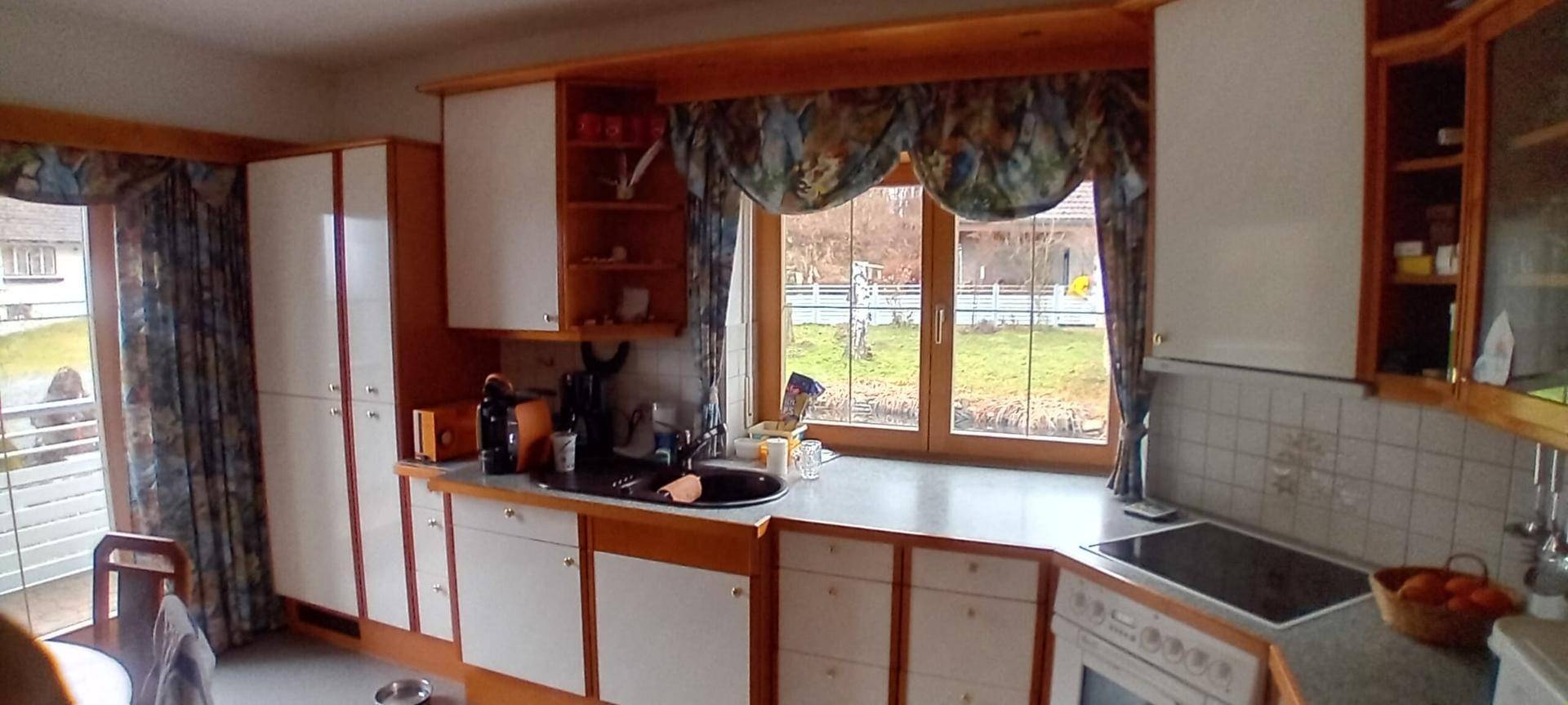 Helle Küche mit Holzschränken, Arbeitsplatte und Blick ins Grüne durch das Fenster.