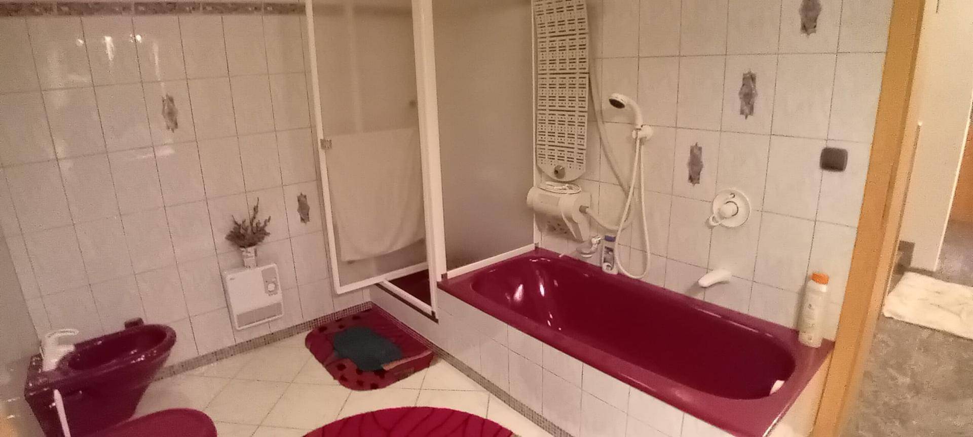 Badezimmer mit roter Badewanne, Bidet und Duschkabine, gefliest in hellem Muster.