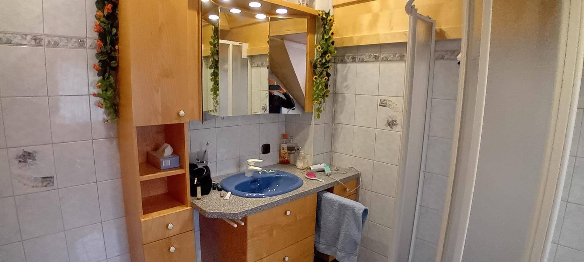 Badezimmer mit blauem Waschbecken, Spiegelschrank und Duschkabine, gefliest in hellem Muster.