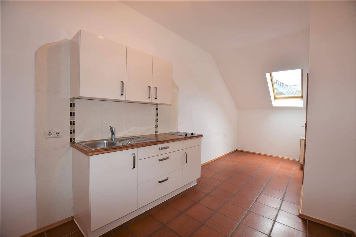 Kleine Küchenzeile mit weißen Schränken, Spüle und Kochfeld unter einem Dachfenster.
