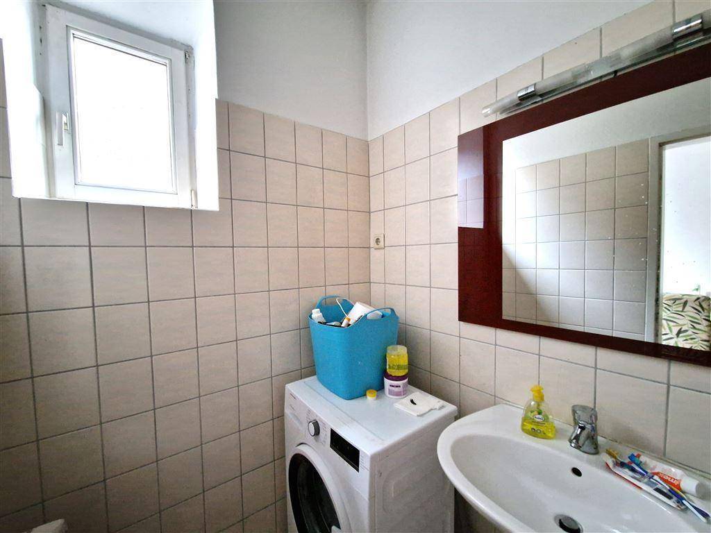 Kleines Badezimmer mit Waschbecken, Spiegel und Waschmaschine, hell gefliest.