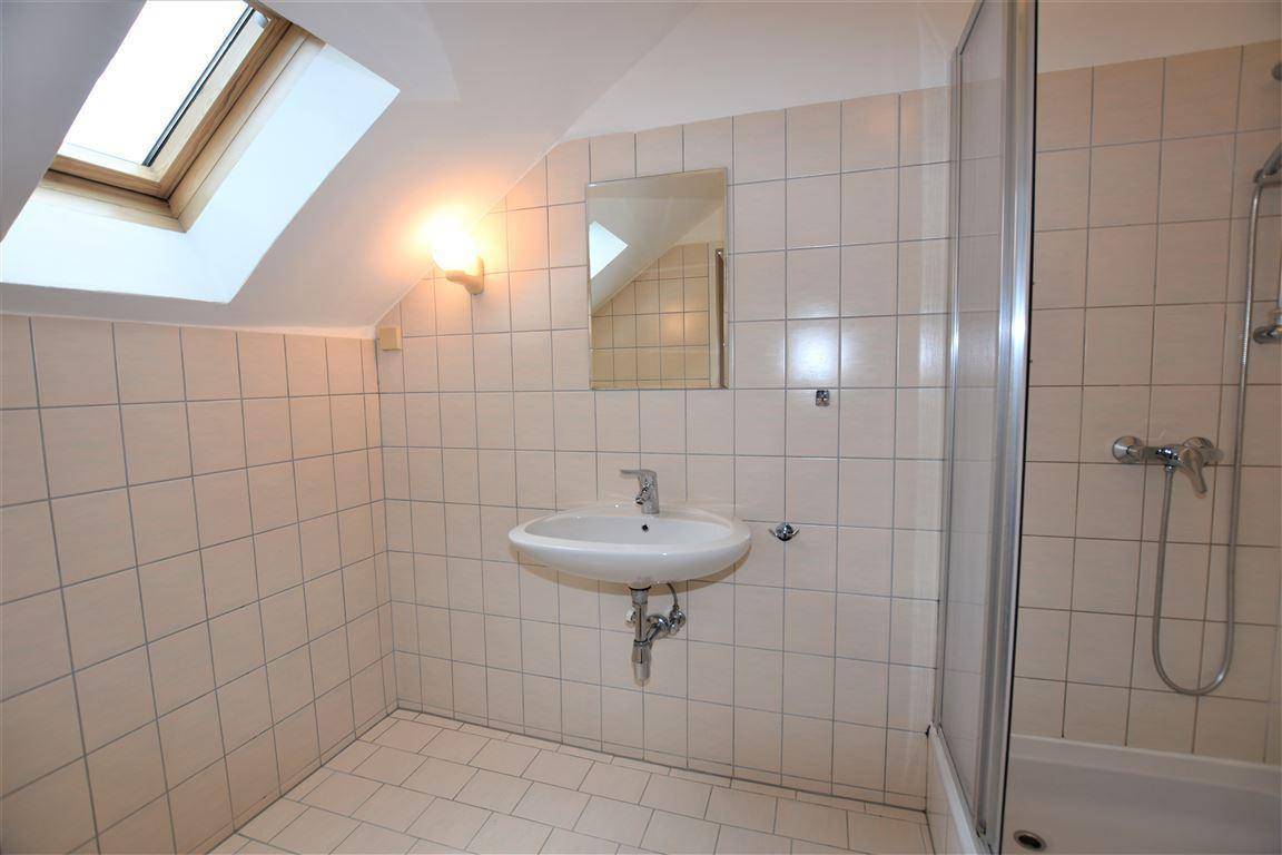 Badezimmer mit hellen Fliesen, Waschbecken und Duschkabine unter einem Dachfenster.