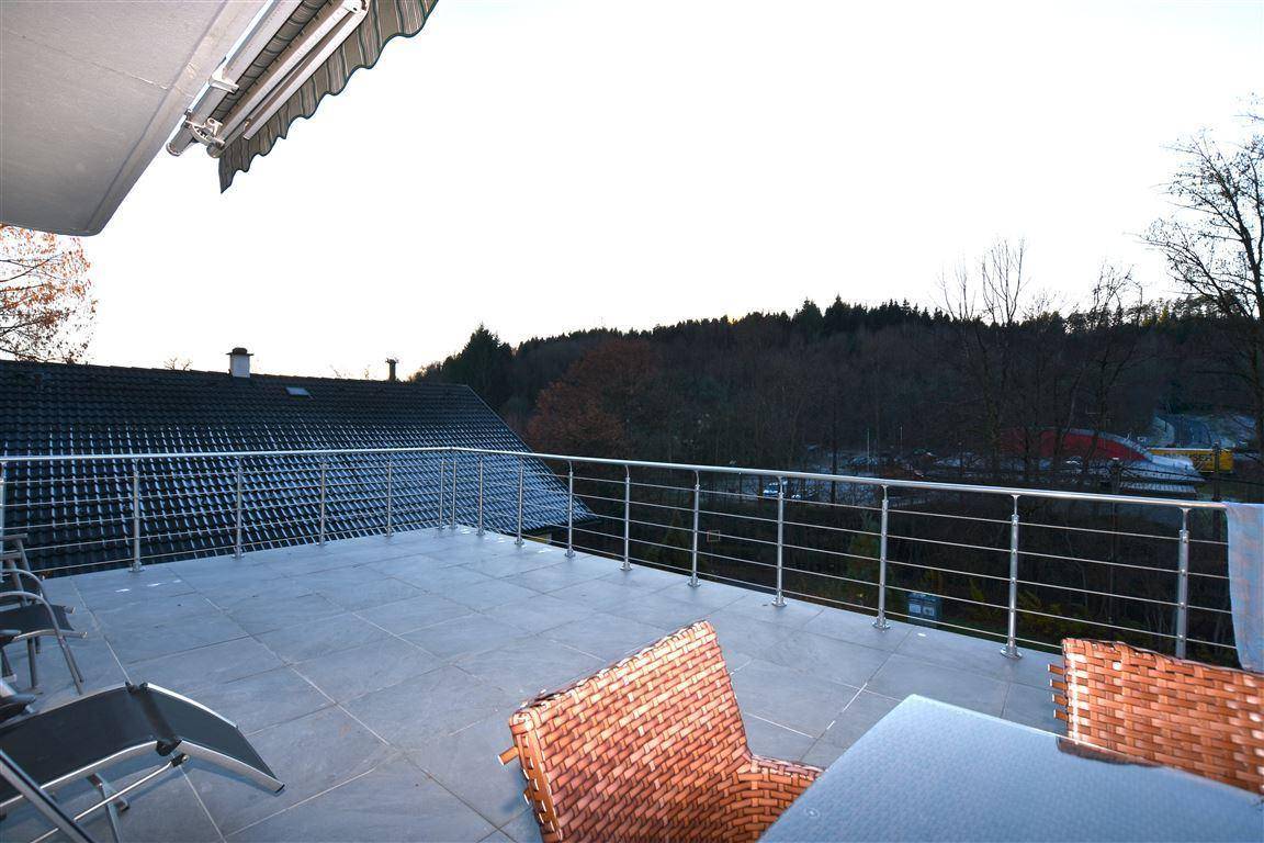 Große geflieste Terrasse mit Metallgeländer, Markise und weitem Blick auf die bewaldete Umgebung.