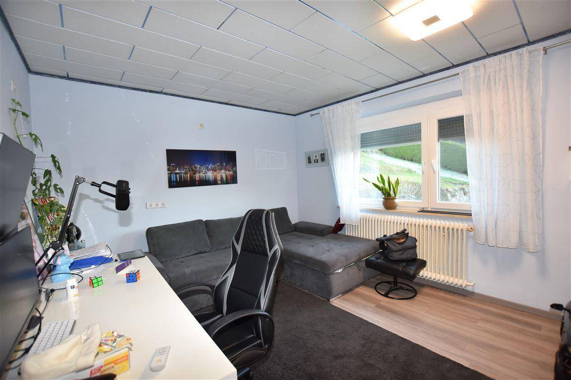 Helles Arbeitszimmer mit Schreibtisch, Sofa und Blick ins Grüne durch das Fenster.