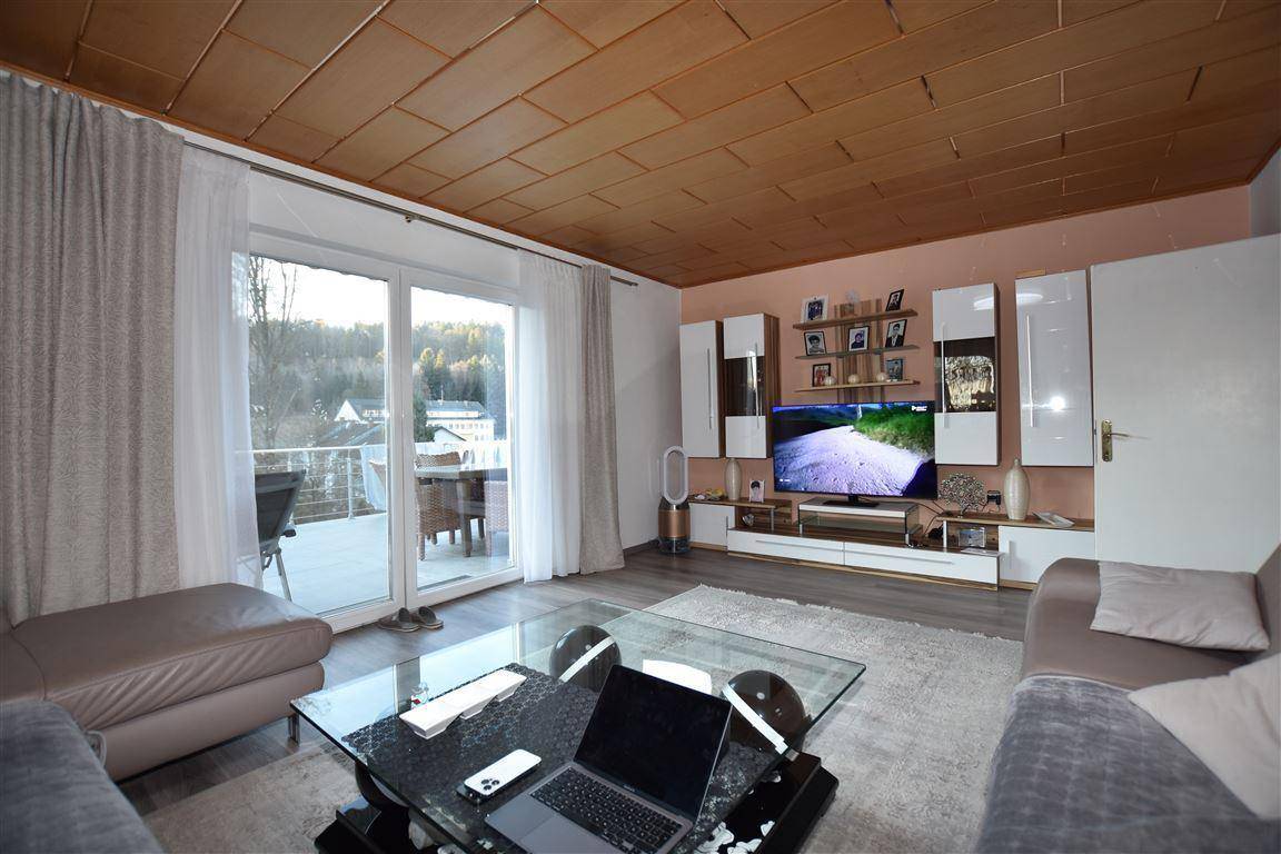 Gemütliches Wohnzimmer mit Zugang zum Balkon, modernem Mediamöbel und Blick ins Grüne.