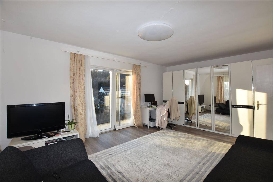 Helles Schlafzimmer mit großem Spiegelschrank, Sofa und Zugang zu einem sonnigen Balkon.