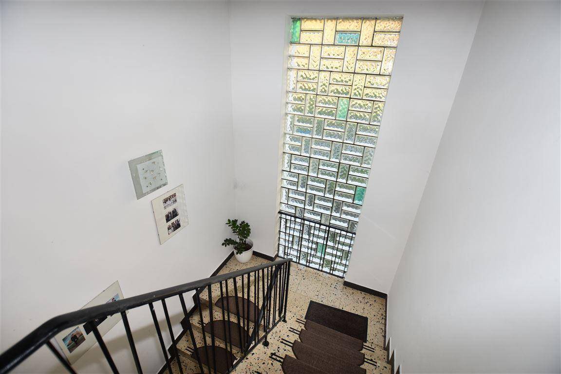 Treppenhaus mit Terrazzoboden, schmiedeeisernem Geländer und farbigem Glasbausteinfenster.
