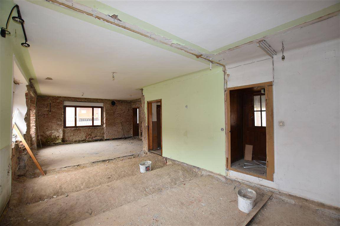 Großer Innenraum in Abrisszustand mit teilweise freigelegten Ziegelwänden und Betonboden, bereit zur Sanierung.