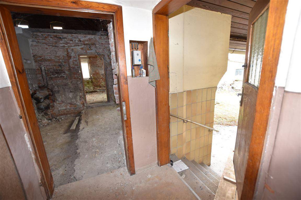 Eingangsbereich mit Holzrahmen und Treppe, die in einen sanierungsbedürftigen Raum führt.