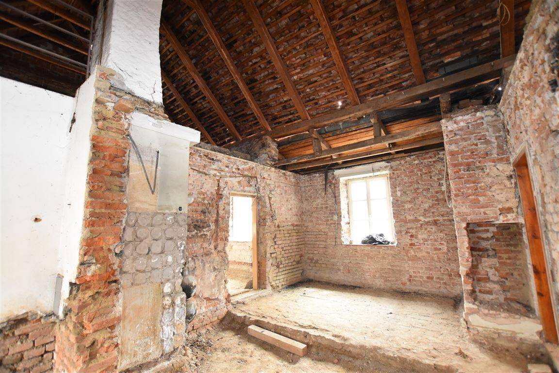 Raum in Abrisszustand mit freigelegten Ziegelwänden und sichtbarer Dachkonstruktion aus Holz.