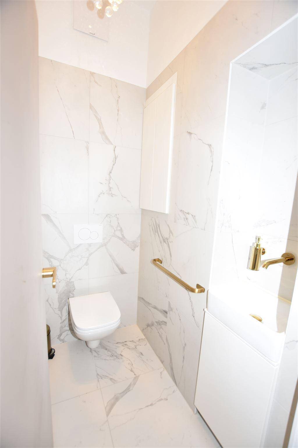 Elegantes WC mit Marmorfliesen, wandhängender Toilette und goldenen Haltegriffen.