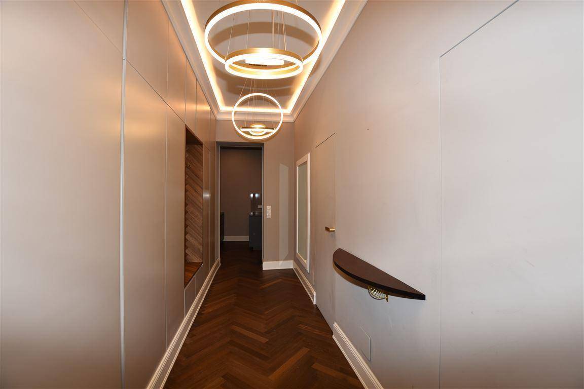 Langer Flur mit elegantem Fischgrätparkett und modernen Deckenleuchten.