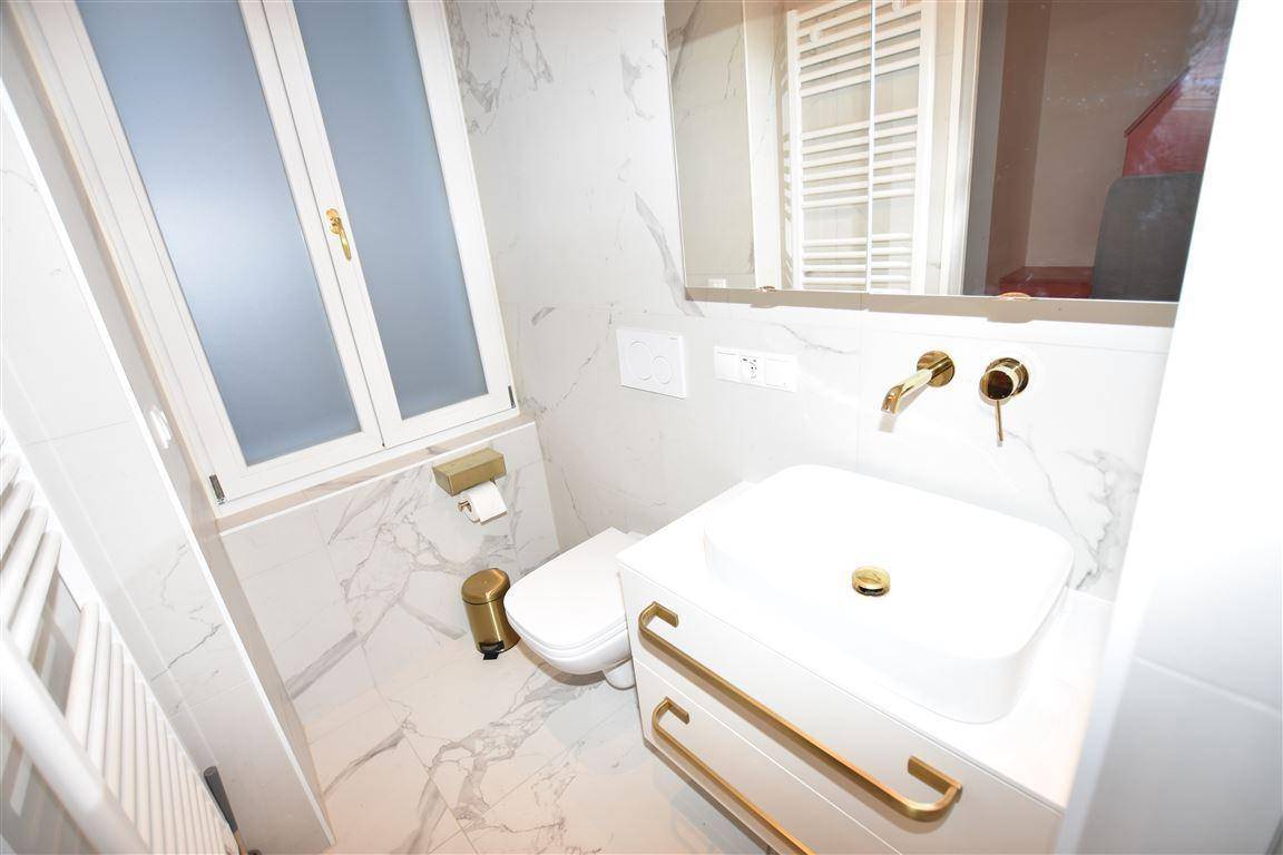 Modernes Badezimmer mit Marmorfliesen, goldenen Armaturen und Fenster.