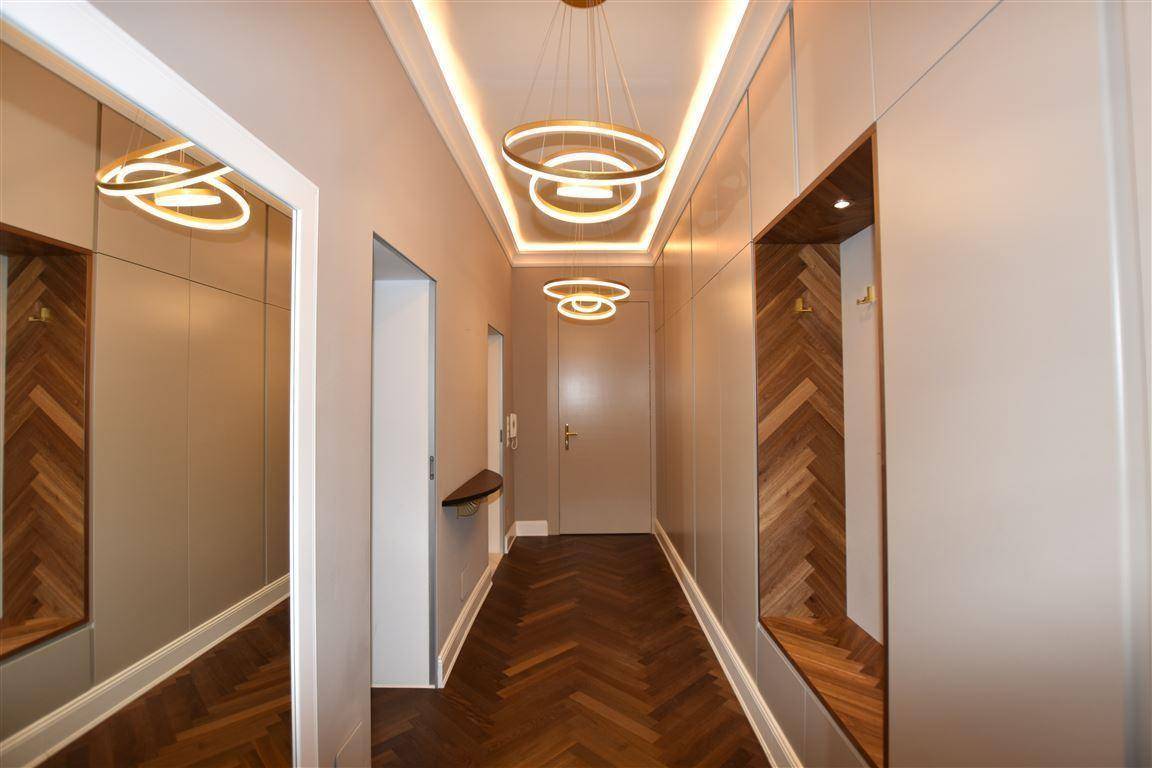 Eleganter Flur mit Fischgrätparkett, modernen Deckenleuchten und integrierter Garderobe.