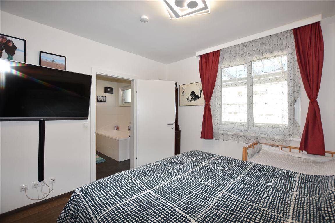 Schlafzimmer mit Holzbett, Fernseher und direktem Zugang zu einem modernen Badezimmer.