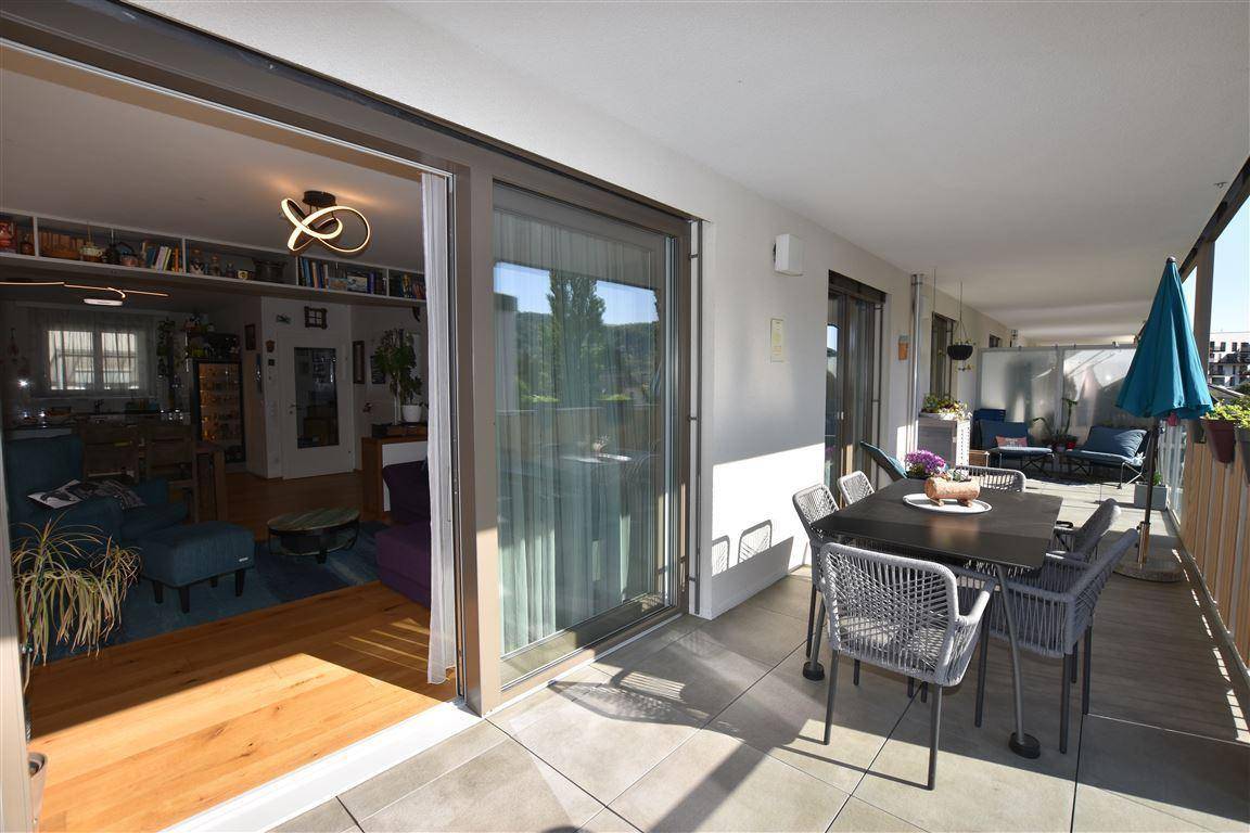 Langer Balkon mit Sitzgelegenheiten, Sonnenschirm und Blick in den Wohnbereich.