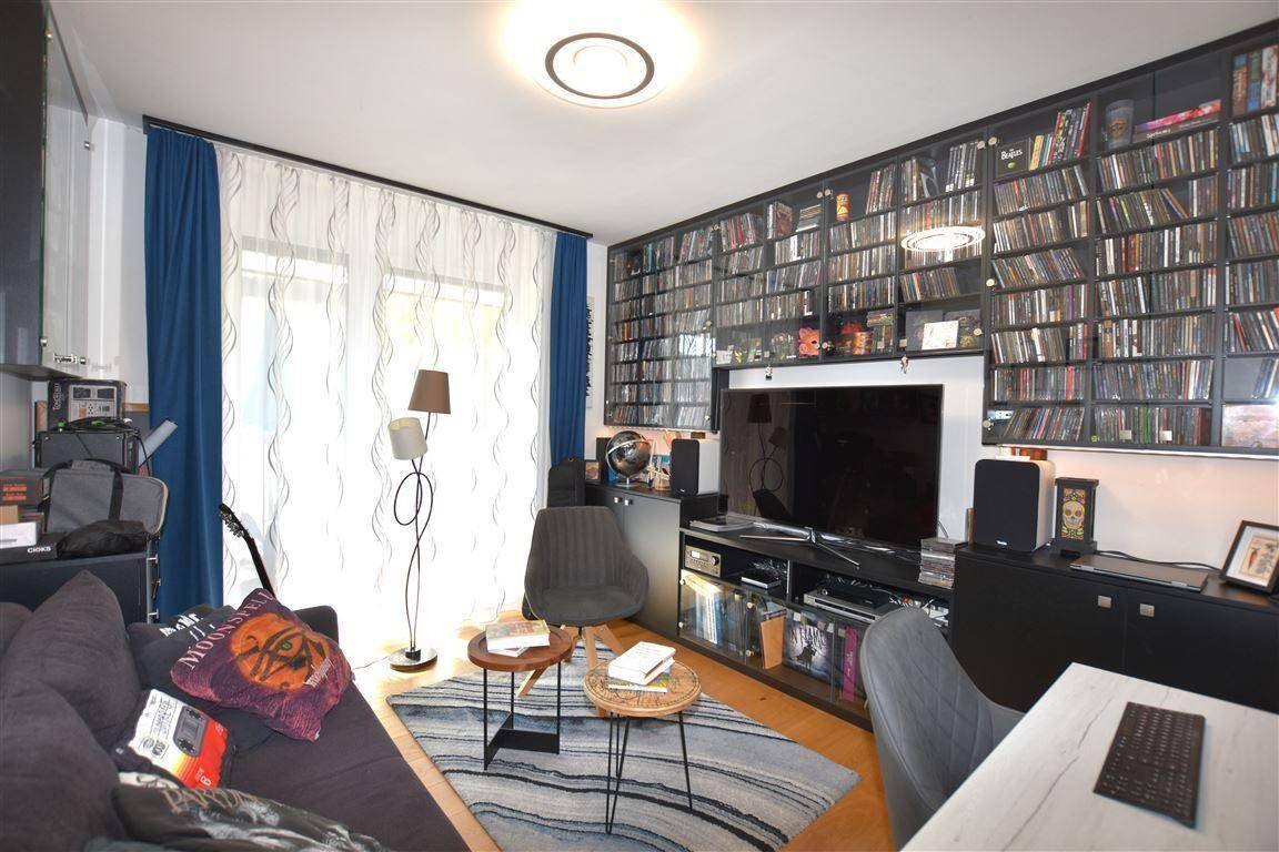 Gemütlicher Wohnbereich mit großem Bücherregal, Sofa und Fenster mit blauen Vorhängen.