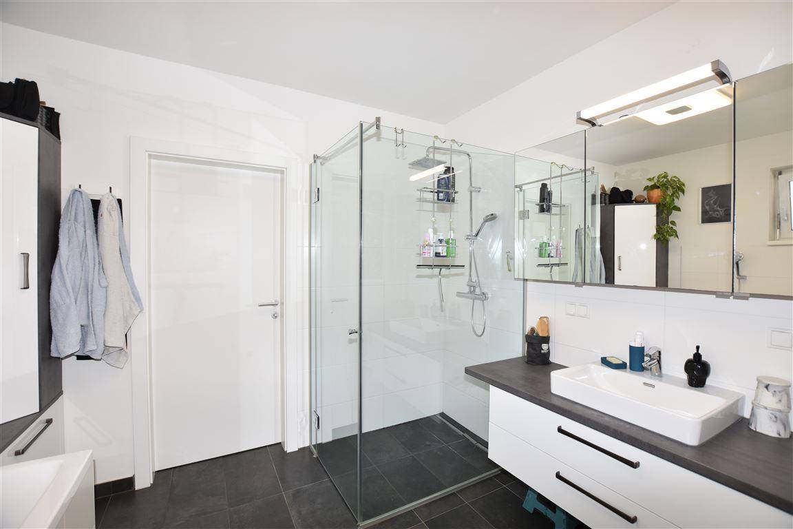 Modernes Badezimmer mit großer Glasdusche, dunklen Fliesen und weißem Waschtisch.