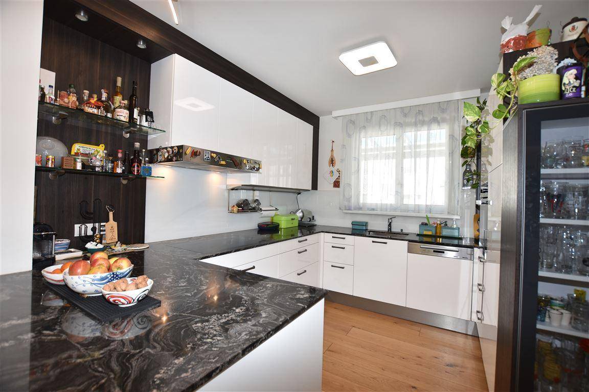 Moderne Küche mit weißen Hochglanzfronten, dunkler Granitarbeitsplatte und Holzboden.