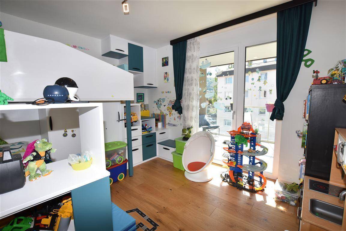 Kinderzimmer mit Hochbett, Spielzeug und großen Fenstern für viel Tageslicht.