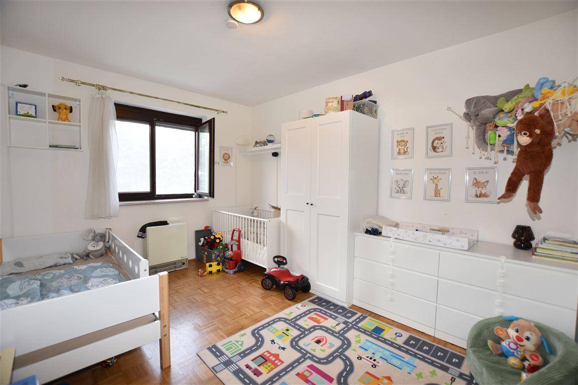 Helles Kinderzimmer mit Holzboden, Babybett, Kleiderschrank und Spielteppich.