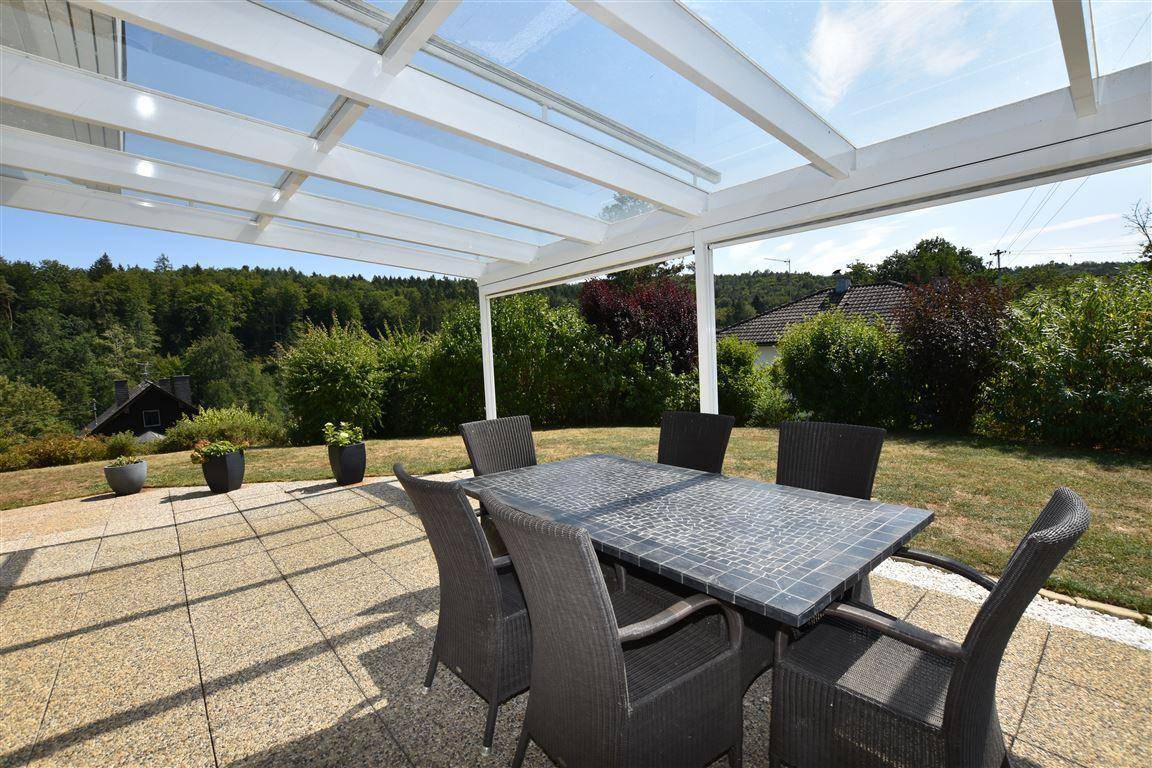 Überdachte Terrasse mit Esstisch und Stühlen, ideal für Mahlzeiten im Freien mit Blick ins Grüne.