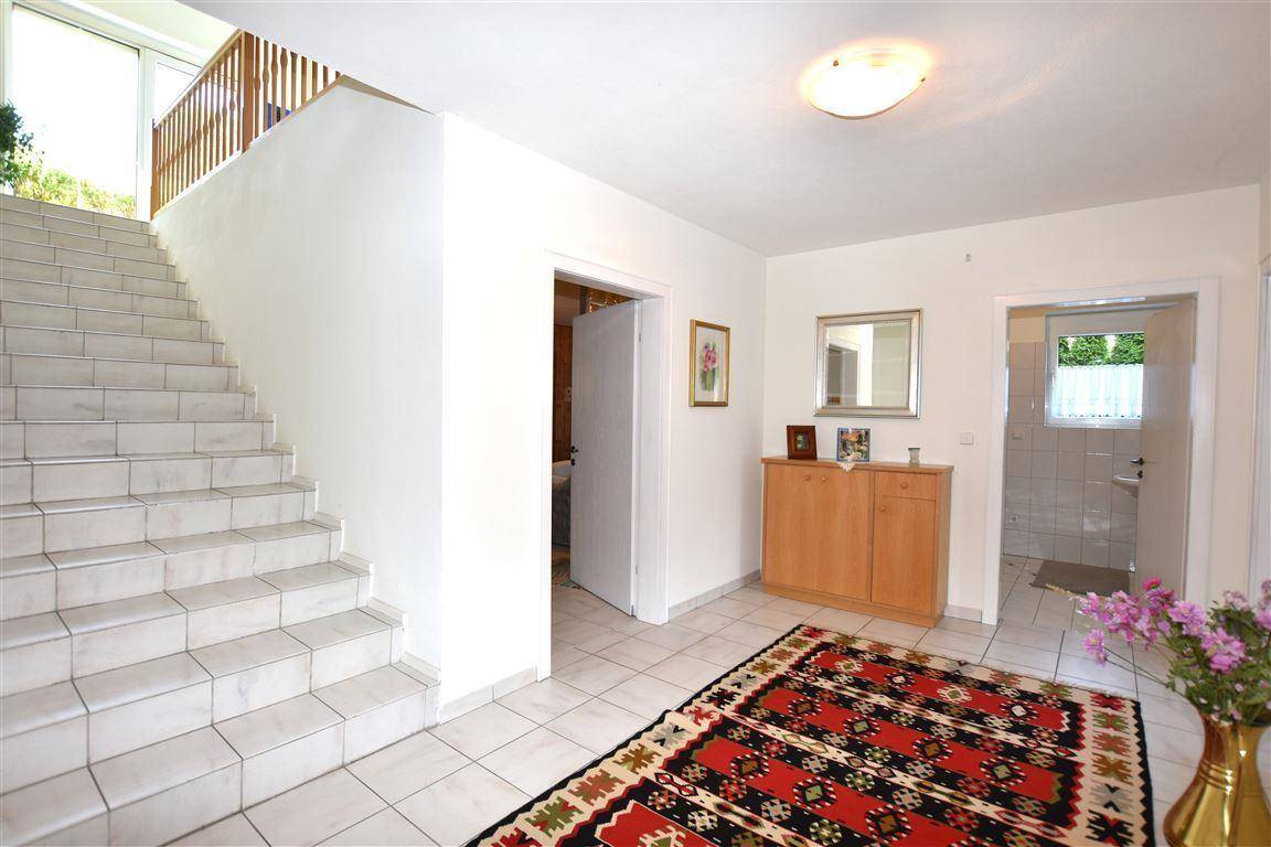 Heller Flur mit gefliester Treppe, Teppich und einem kleinen Holzschrank.
