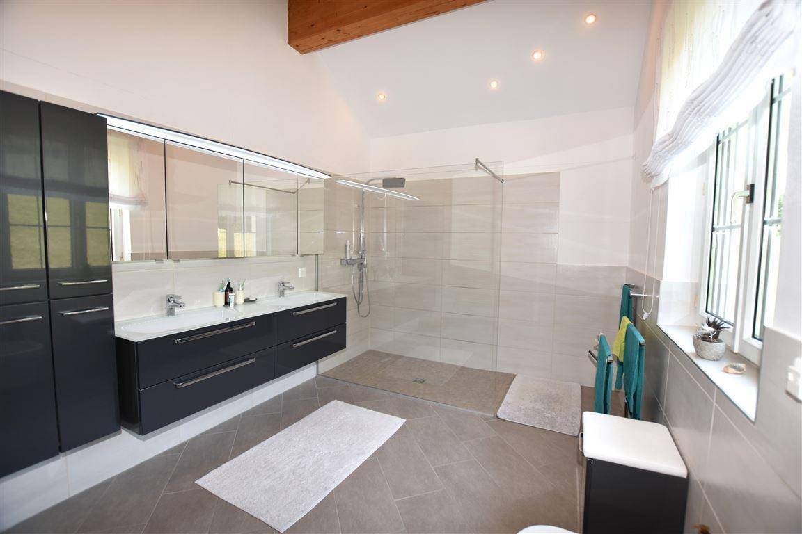 Modernes Badezimmer mit Doppelwaschbecken, großer begehbarer Dusche und Fenster für Tageslicht.