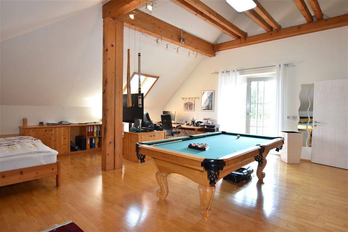 Vielseitiger Raum im Dachgeschoss mit sichtbaren Holzbalken, Billardtisch und Zugang zum Balkon.