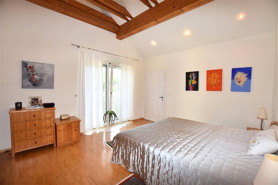Helles Schlafzimmer mit Doppelbett, Holzbalken an der Decke und direktem Zugang zum Balkon.