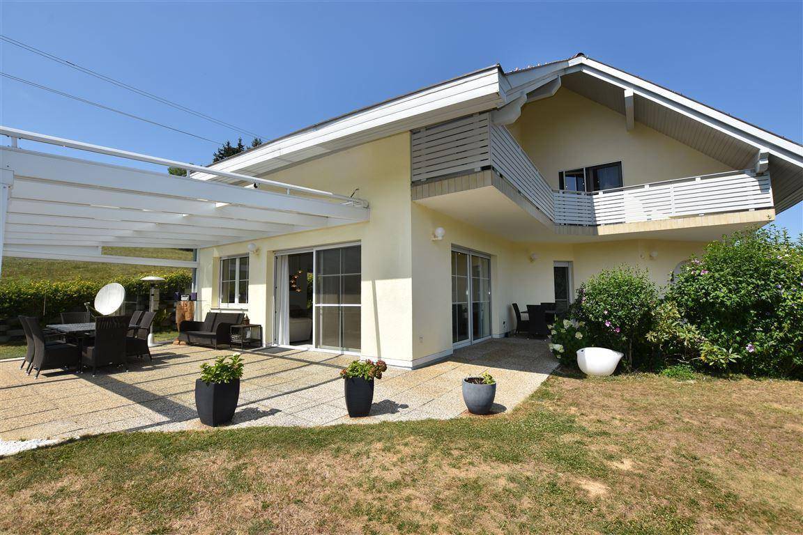 Hausfassade mit großer überdachter Terrasse, Gartenbereich und mehreren Zugängen zum Innenraum.