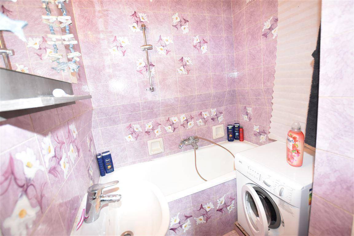 Badezimmer mit lila Fliesen, Badewanne und Waschmaschine.