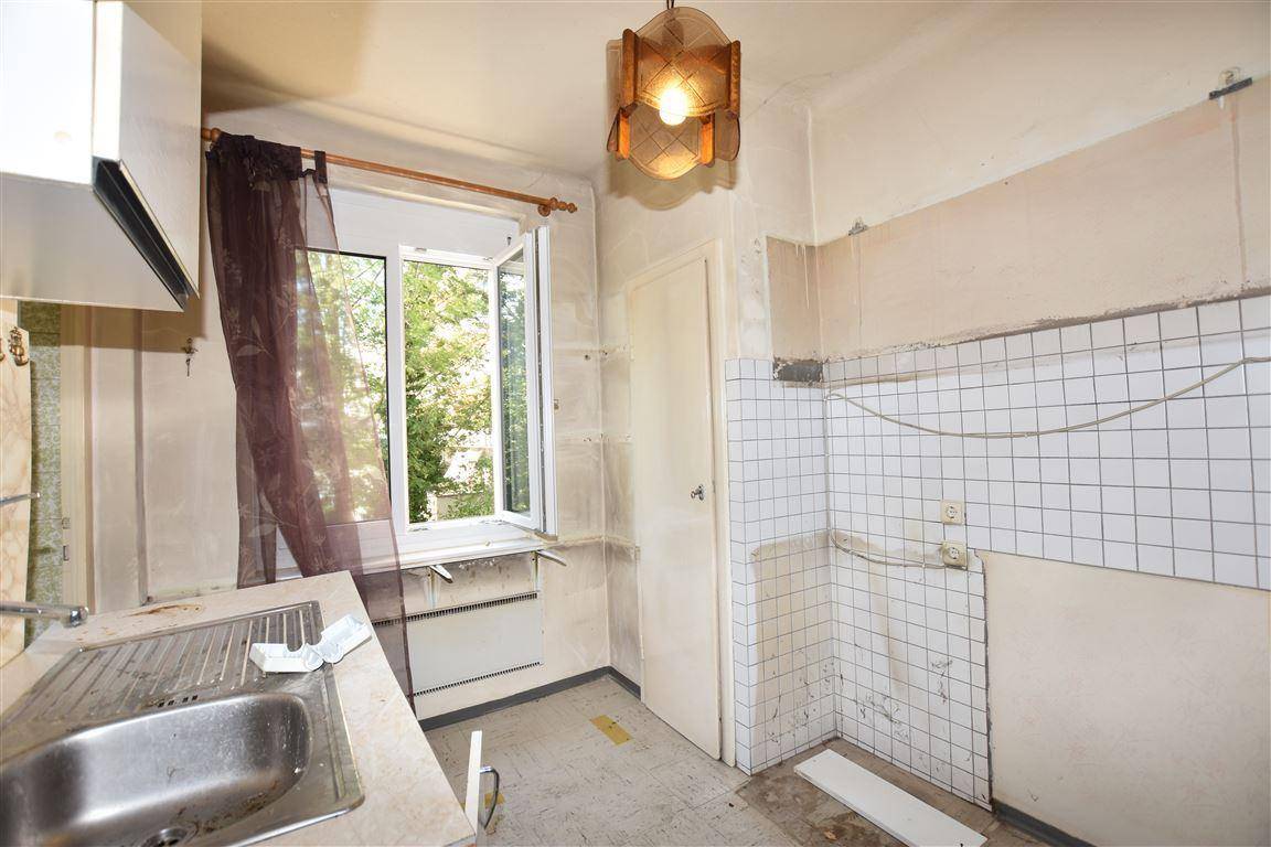 Renovierungsbedürftige Küche mit Spülbecken, gefliesten Wänden und Fenster mit Blick ins Grüne.