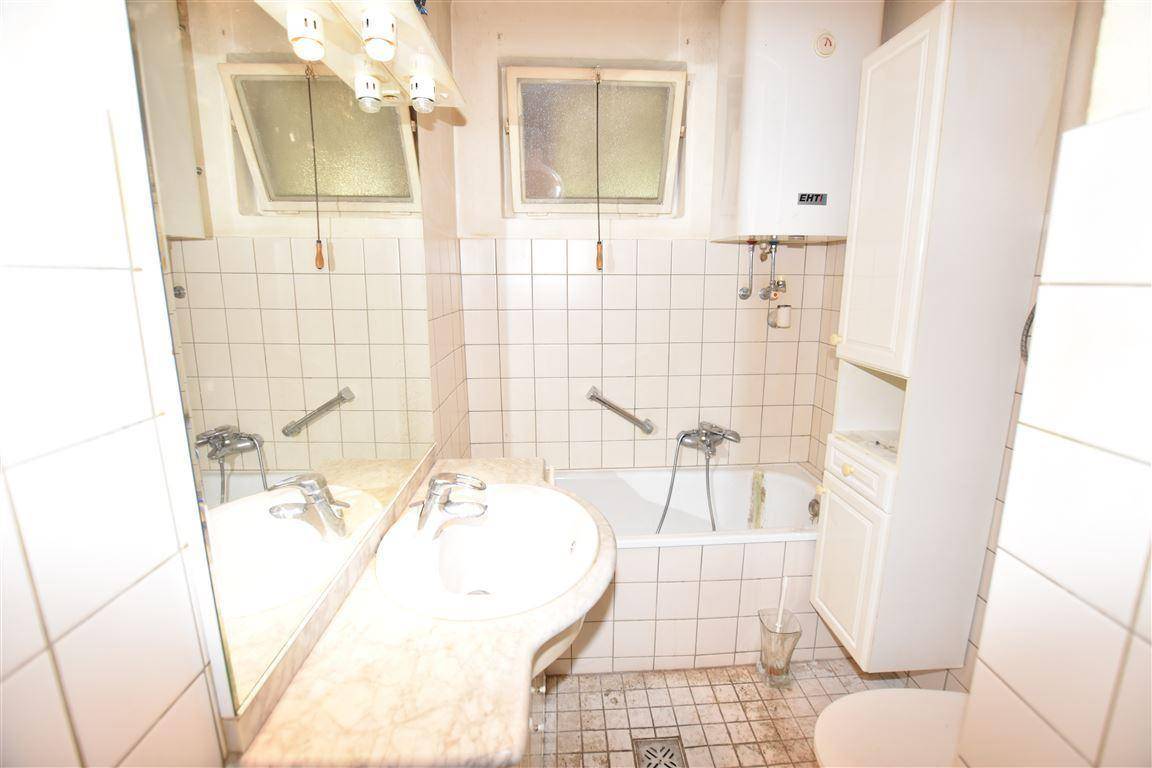 Badezimmer mit Badewanne, Waschbecken und Spiegel, ausgestattet mit Fliesen und zwei kleinen Fenstern.