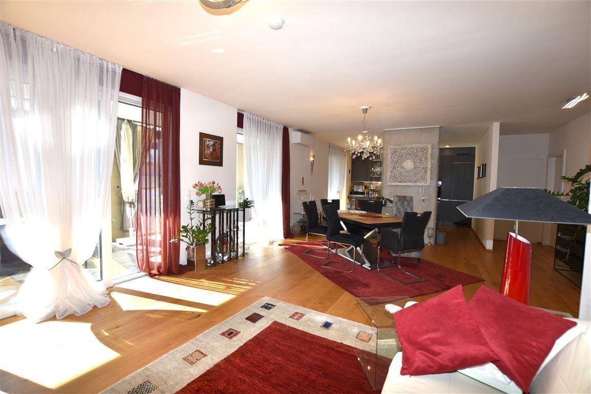 Lichtdurchfluteter Wohn-Essbereich mit Holzboden, elegantem Esstisch und Zugang zu großen Fenstern.