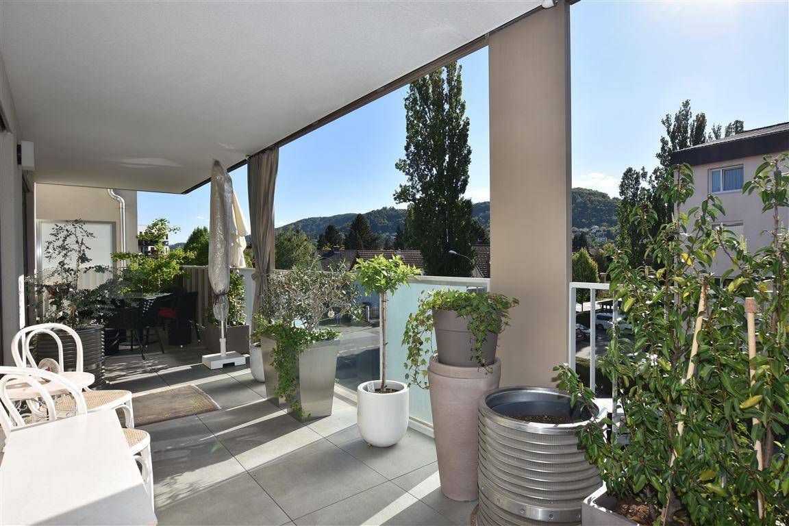 Geräumiger Balkon mit Sitzgelegenheiten, vielen Pflanzen und weitem Blick auf die grüne Umgebung.