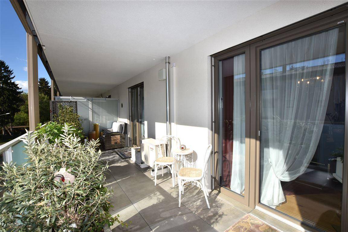 Heller Balkon mit Sitzgelegenheiten, Pflanzen und großen Glasfenstern zum Innenraum.