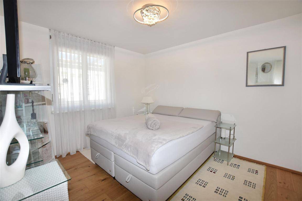 Helles Schlafzimmer mit Doppelbett, Holzboden und einem Fenster mit leichten Vorhängen.