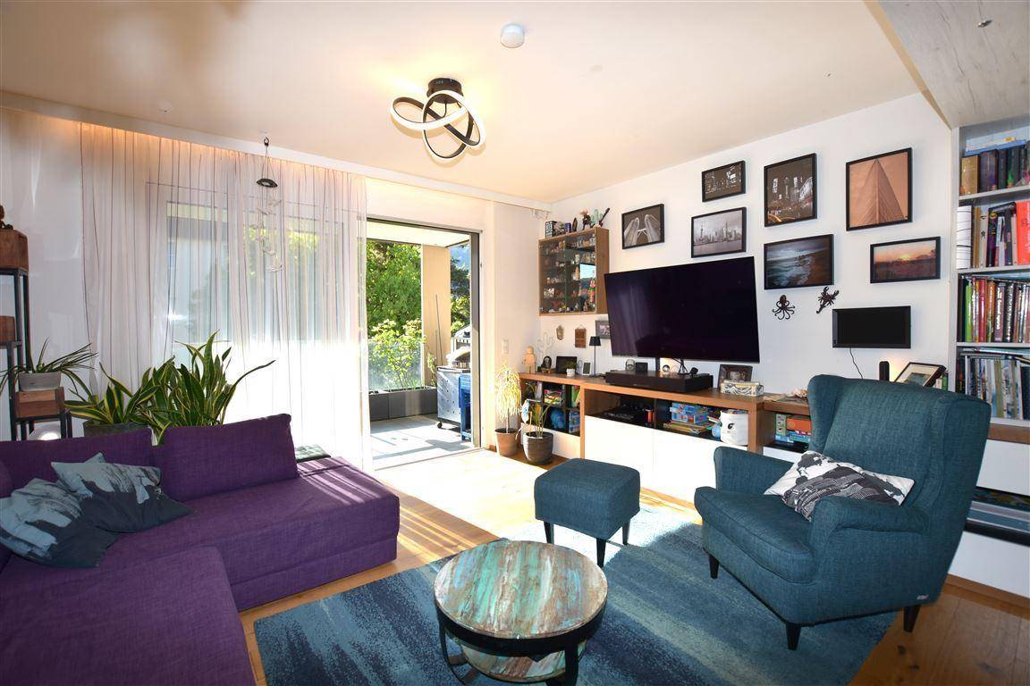 Gemütliches Wohnzimmer mit lila Sofa, Fernseher und direktem Zugang zum sonnigen Balkon.