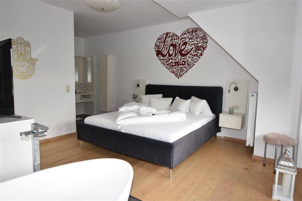 Geräumiges Schlafzimmer mit großem Bett, Holzboden und einer freistehenden Badewanne im Raum.
