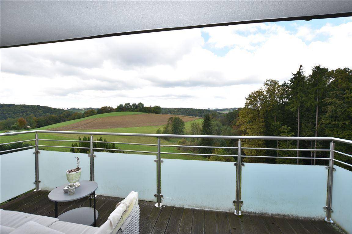 Balkon mit Glasgeländer und weitem Blick über die grüne Landschaft und Felder.