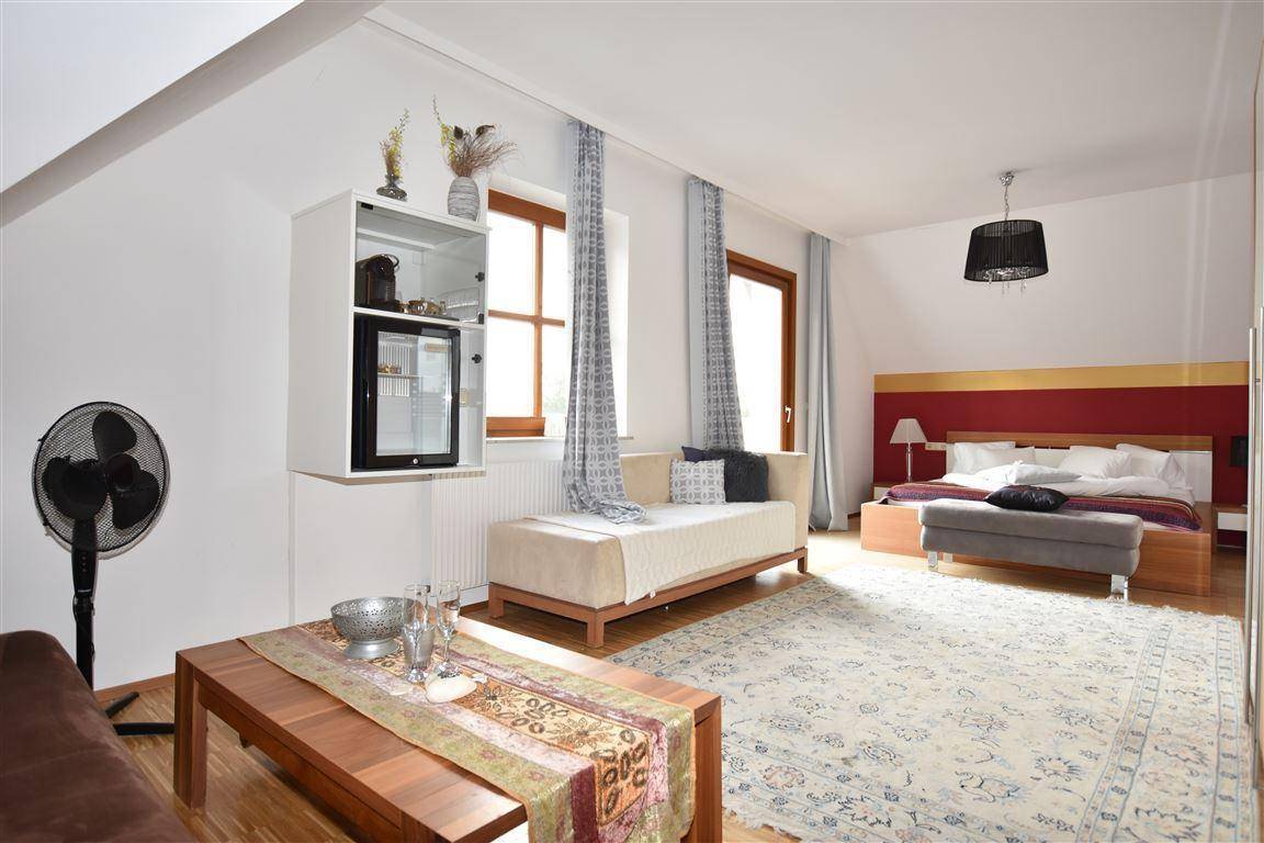 Helles Schlafzimmer mit Doppelbett, Tagesbett, Minibar und Teppichboden unter einer Dachschräge.